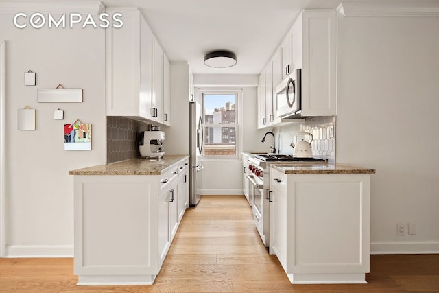 kitchen with sink, light stone counters, stainless steel appliances, light hardwood / wood-style floors, and white cabinets