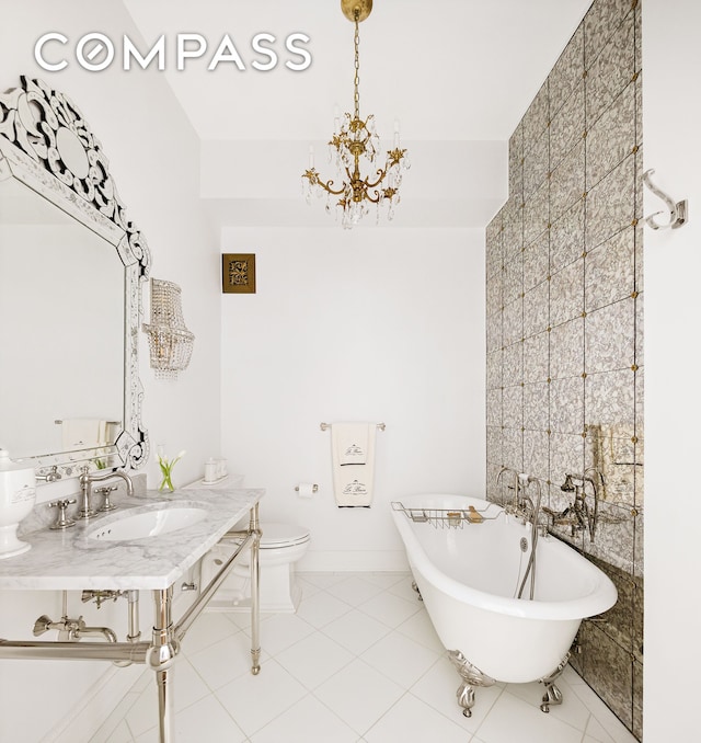 bathroom featuring baseboards, a freestanding tub, toilet, tile patterned flooring, and a notable chandelier