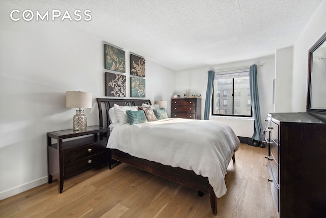 bedroom featuring baseboards, light wood finished floors, and a textured ceiling