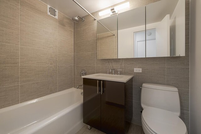 full bathroom featuring toilet, tile walls, vanity, tiled shower / bath combo, and decorative backsplash