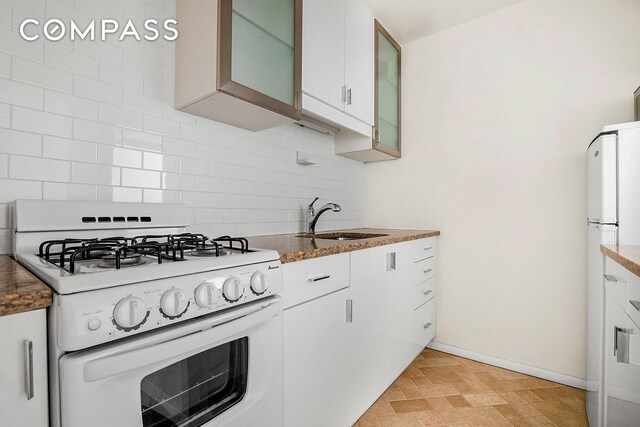 kitchen with sink, stone countertops, white cabinets, white appliances, and backsplash