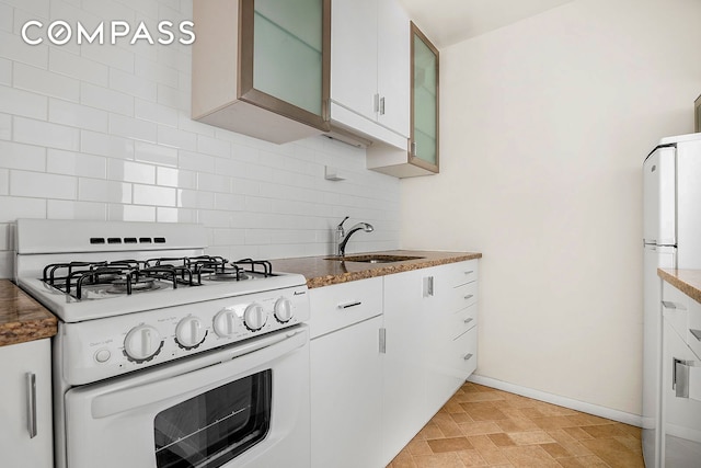 kitchen featuring baseboards, decorative backsplash, white appliances, white cabinetry, and a sink