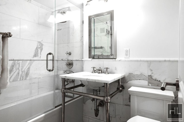 bathroom featuring tile walls, toilet, combined bath / shower with glass door, and a sink