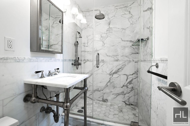 bathroom featuring a sink, a marble finish shower, and tile walls