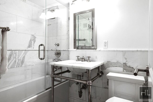 full bathroom with a sink, toilet, tile walls, and combined bath / shower with glass door