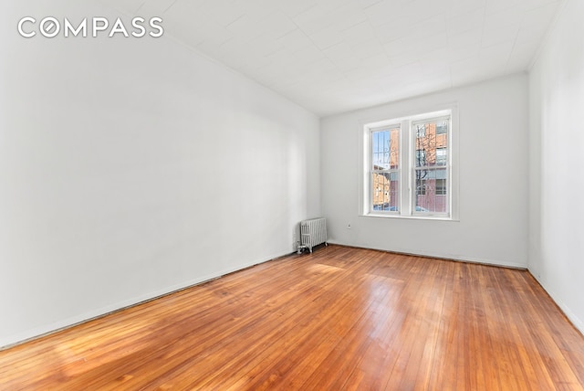 unfurnished room featuring radiator heating unit and hardwood / wood-style flooring