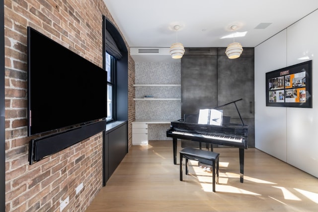 sitting room featuring brick wall, light wood finished floors, visible vents, and an accent wall