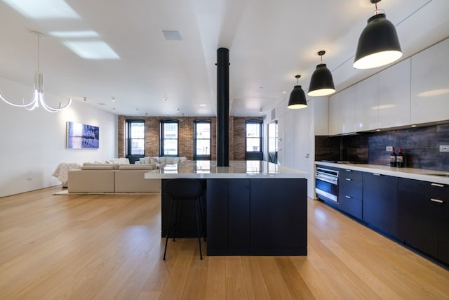 kitchen featuring stainless steel oven, hanging light fixtures, a kitchen island, white cabinets, and backsplash