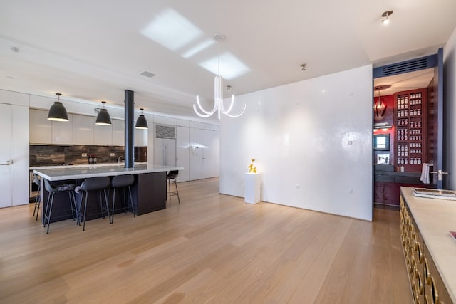 kitchen with decorative light fixtures, white cabinets, a kitchen breakfast bar, a center island with sink, and light wood-type flooring