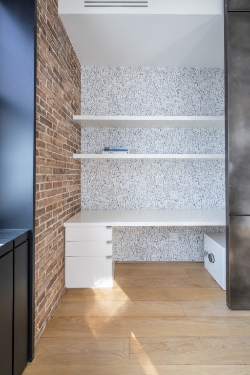 staircase with brick wall, built in desk, and hardwood / wood-style floors