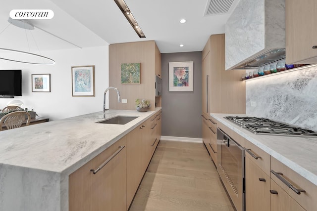 kitchen featuring light brown cabinetry, wall chimney range hood, a sink, and visible vents