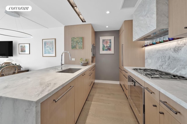 kitchen featuring a sink, wall chimney range hood, light brown cabinets, and recessed lighting