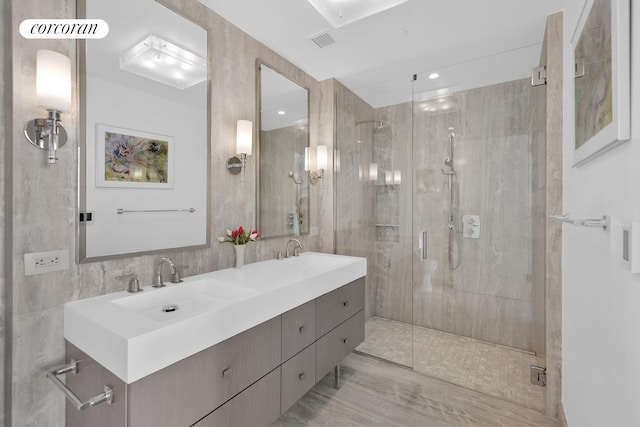 bathroom with a shower stall, double vanity, and tile walls