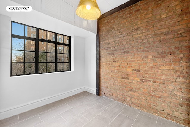 unfurnished room with baseboards, visible vents, and brick wall