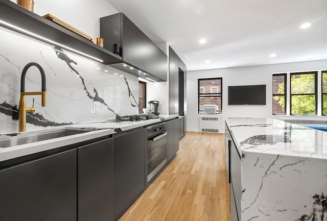 kitchen featuring radiator, oven, decorative backsplash, light stone countertops, and light hardwood / wood-style flooring