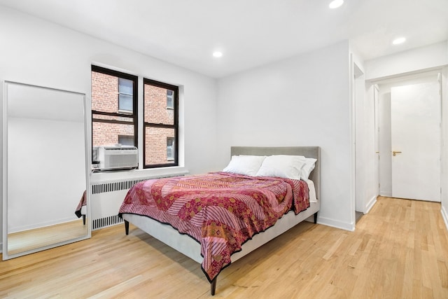 bedroom featuring cooling unit, radiator heating unit, and light hardwood / wood-style floors