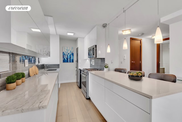 kitchen featuring sink, hanging light fixtures, stainless steel appliances, light hardwood / wood-style floors, and white cabinets