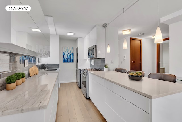 kitchen with appliances with stainless steel finishes, light wood-style floors, white cabinets, a sink, and modern cabinets