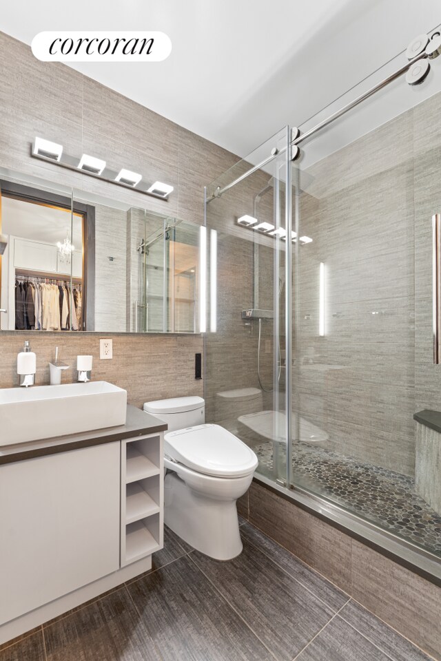bathroom featuring tile walls, toilet, a stall shower, vanity, and a chandelier