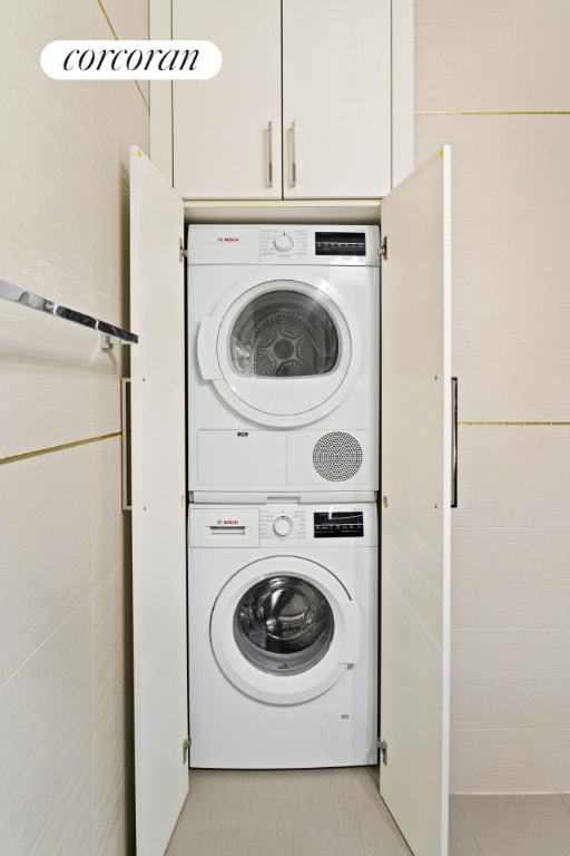 clothes washing area featuring light tile patterned flooring, stacked washer / drying machine, and tile walls