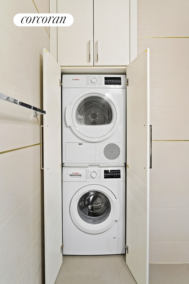 clothes washing area featuring light tile patterned floors, stacked washer / dryer, laundry area, and tile walls