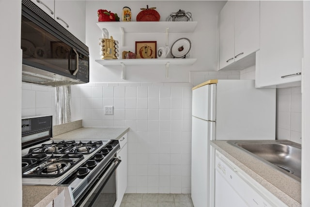 kitchen featuring light tile patterned flooring, sink, tile walls, white cabinets, and white appliances