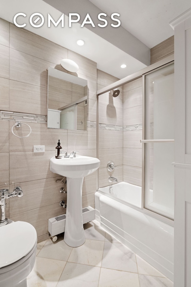 bathroom with tile walls, toilet, combined bath / shower with glass door, and a sink