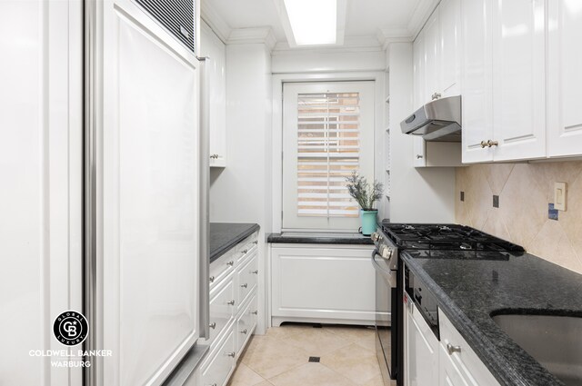 kitchen featuring dark stone countertops, ornamental molding, stainless steel range with gas stovetop, decorative backsplash, and white cabinets