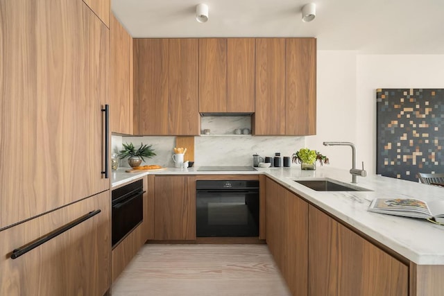 kitchen with tasteful backsplash, light stone countertops, sink, and black appliances