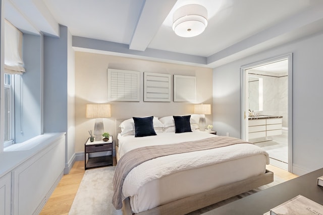 bedroom featuring light wood finished floors, beam ceiling, ensuite bathroom, and baseboards