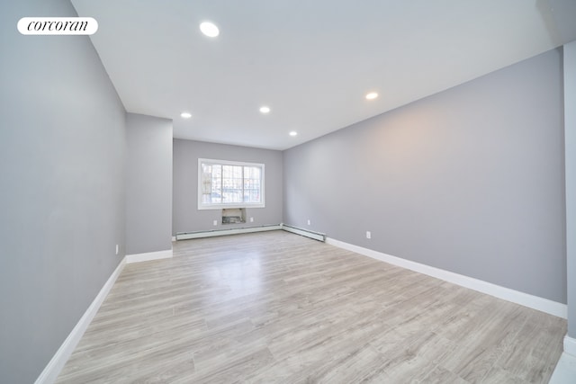 unfurnished room featuring a baseboard heating unit and light hardwood / wood-style floors