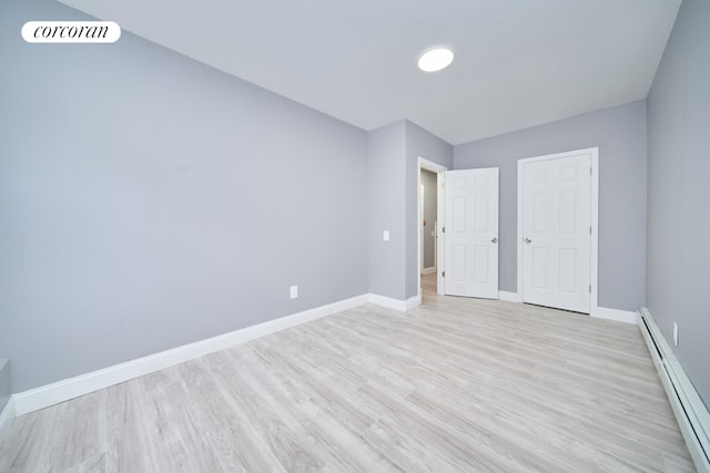 unfurnished bedroom with baseboard heating and light hardwood / wood-style floors