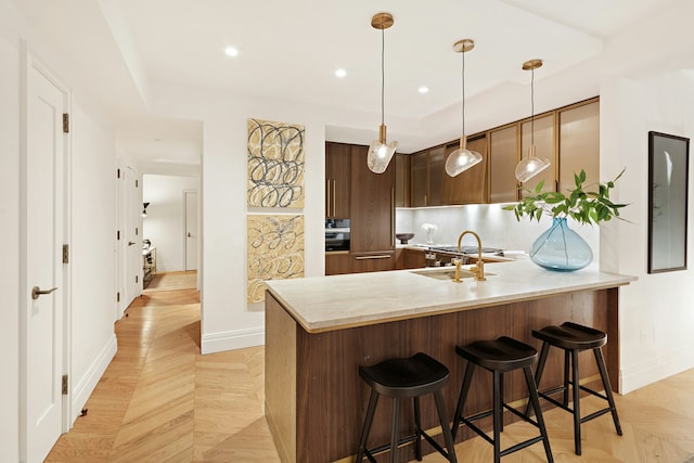 kitchen with a sink, a peninsula, light countertops, a kitchen bar, and baseboards
