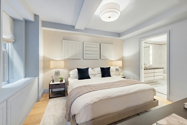 bedroom featuring ensuite bathroom, baseboards, beam ceiling, and light wood-style floors