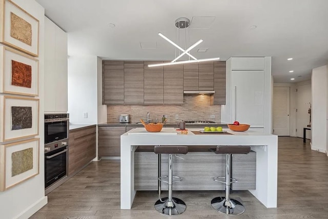 kitchen with pendant lighting, backsplash, wood-type flooring, and a breakfast bar