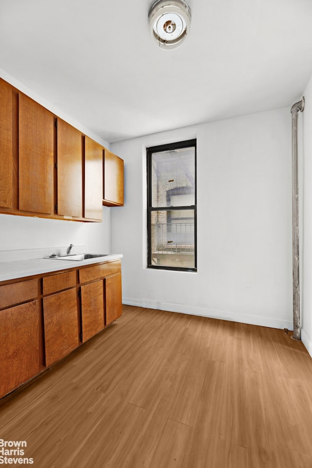 kitchen with a sink, baseboards, light countertops, light wood finished floors, and brown cabinetry