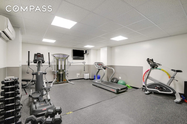 exercise area with a drop ceiling, an AC wall unit, and baseboards