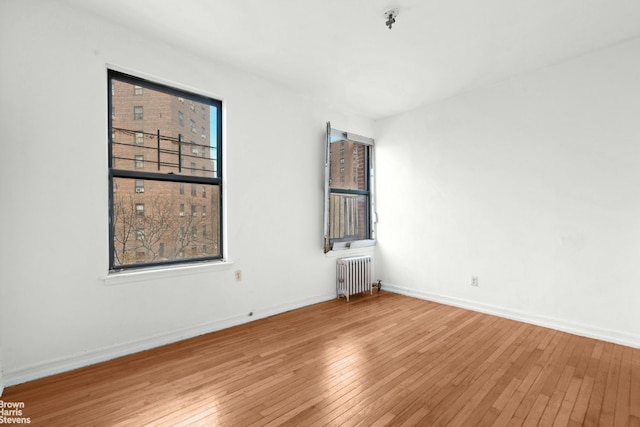 spare room with hardwood / wood-style flooring, a healthy amount of sunlight, and radiator heating unit