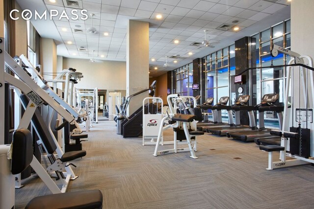 gym featuring carpet flooring, ceiling fan, and a towering ceiling