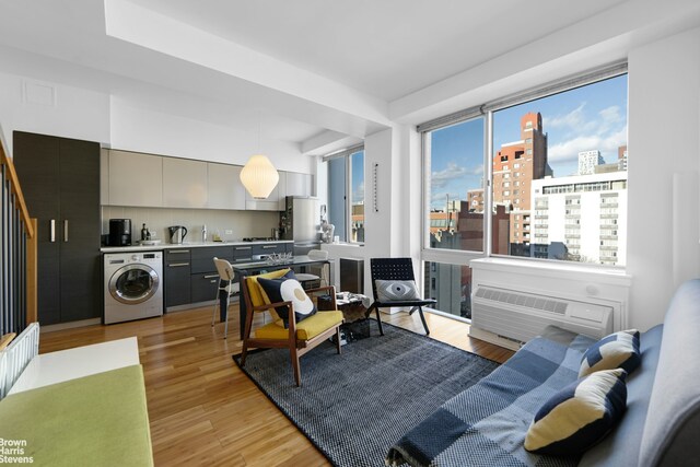 living room with washer / dryer, a wall mounted AC, and light wood-type flooring