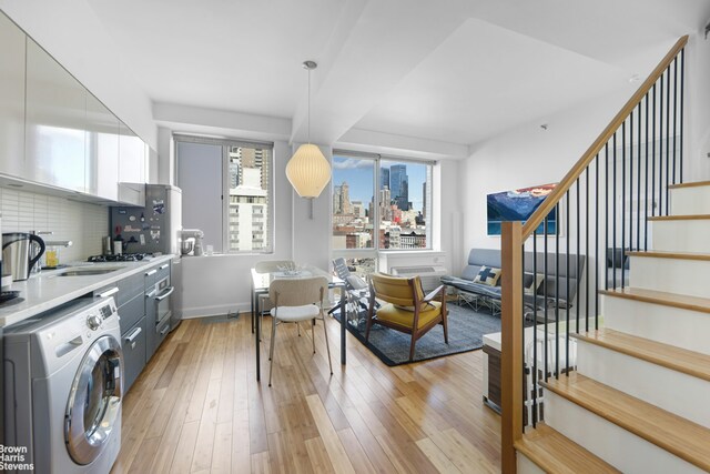 kitchen featuring pendant lighting, gray cabinets, backsplash, light hardwood / wood-style floors, and washer / dryer