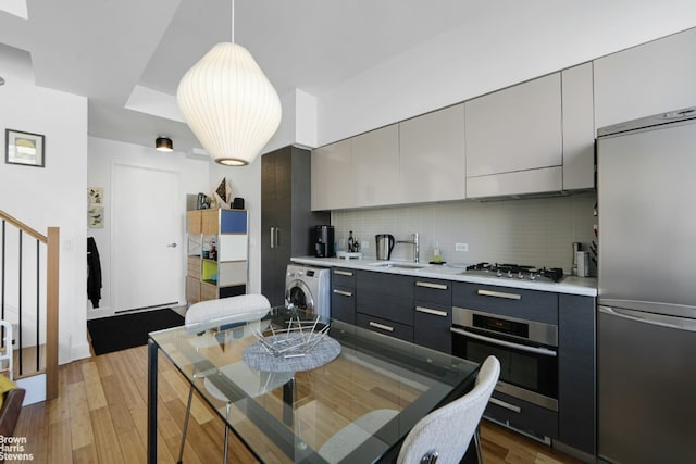 kitchen featuring sink, gray cabinetry, hanging light fixtures, appliances with stainless steel finishes, and washer / clothes dryer