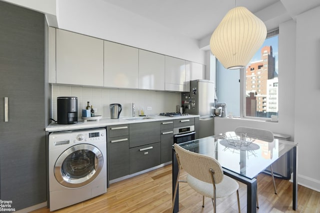 kitchen with washer / dryer, sink, gray cabinetry, decorative light fixtures, and light hardwood / wood-style floors