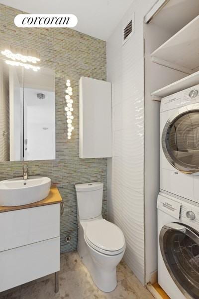 bathroom featuring visible vents, stacked washer and dryer, vanity, and toilet