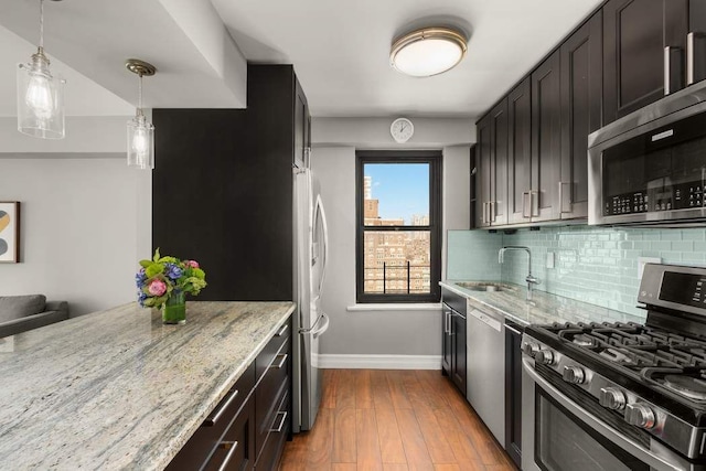 kitchen with sink, hardwood / wood-style flooring, stainless steel appliances, light stone counters, and tasteful backsplash