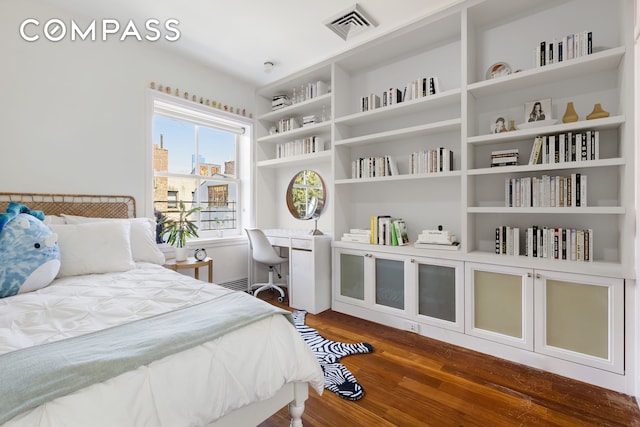 bedroom with visible vents, built in study area, and wood finished floors