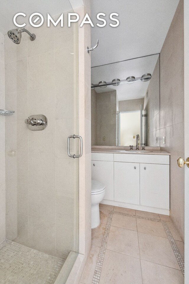 bathroom with vanity, toilet, a shower with shower door, and tile patterned flooring