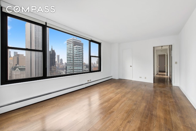 117 E 57th St Unit 35D, New York City, NY 10022 - empty room featuring a baseboard radiator, wood finished floors, healthy amount of natural light, and a skyline view