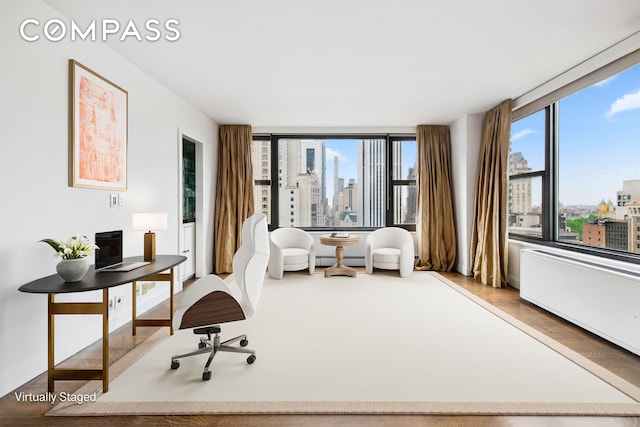 living area featuring baseboards, wood finished floors, a view of city, a wall of windows, and a baseboard heating unit