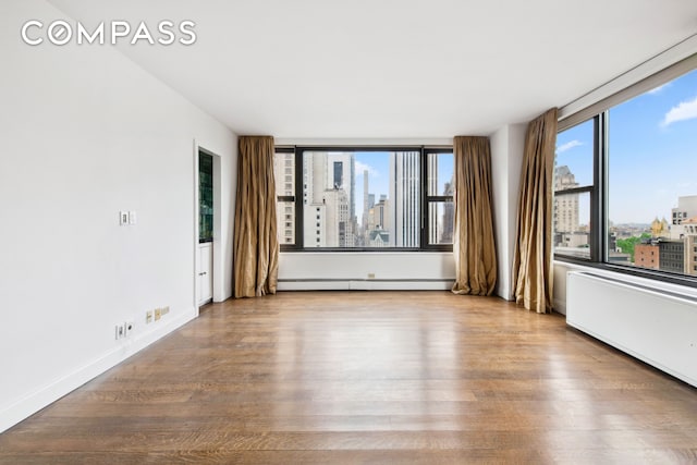 empty room with baseboards, baseboard heating, a city view, and wood finished floors